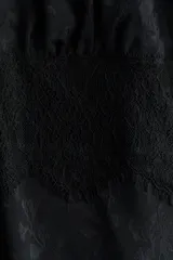 Top negro de tejido jacquard con leve brillo, escote en V y copas fruncidas. Presenta un panel transparente de encaje en el torso y ribetes de encaje decorativos en el escote y los breteles.