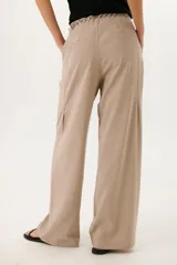 Pantalón de vestir color beige, de corte palazzo y tiro alto. Incluye cinturón de cadena plateada.