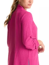 Blusa de tejido piqué color fucsia, con escote en V y pliegue central delantero. Presenta mangas largas con sistema de ajuste mediante presilla y botón, y tajos laterales en el ruedo.