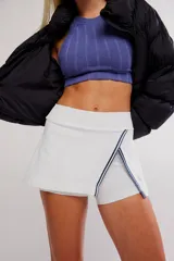 Skort deportivo blanco de tiro alto, con diseño cruzado en el frente y ribetes en contraste azul oscuro, que incluye short interno incorporado.