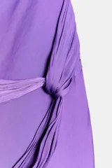 Vestido midi de satén color lila, con cuello halter y tirantes finos. Presenta un detalle de nudo en la cintura y espalda descubierta.
