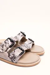 Sandalias de cuero color negro con dos tiras anchas sobre el empeine, cada una con hebillas metálicas ajustables y detalles de tachas plateadas. La suela es de cuero con un borde de color madera.