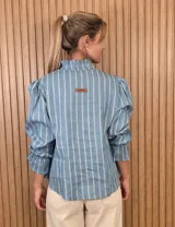 Blusa rosada de algodón con delicados bordados florales blancos, escote en V con cuello elevado y volados, y mangas largas con puños acampanados.