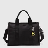 Tote bag de diseño rectangular en color negro, confeccionado en material resistente. Presenta asas de mano fijas y una correa ajustable extraíble, ambas con el logo de la marca estampado. Incluye un dije colgante con la letra B en color amarillo y cierre superior.