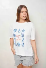 Remerón de algodón color blanco, de corte oversize, manga corta y cuello redondo. Presenta un estampado central con ilustraciones de caracoles y conchas marinas en azul, junto con el texto "Meet me by the sea" en tono rojizo.