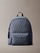 Mochila de poliéster reciclado con estampado de logo jacquard en tonos azul y gris. Presenta asa de mano superior, correas acolchadas ajustables, cierre de cremallera y bolsillo frontal con cremallera.