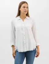 Camisa de tencel color blanco, con cuello camisero, cierre frontal de botones y dos bolsillos en el pecho. Presenta mangas largas con presilla para regular el largo y ruedo con detalle de flecos.