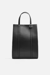 Bolso tipo shopper color negro, con compartimento principal con cierre mediante imán, bolsillo interior con cierre, detalle de arnés en la parte delantera, dos asas de mano y asa de hombro ajustable y extraíble.
