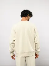 Buzo de felpa color crema, con cuello redondo, manga larga tipo raglán y puños y dobladillo acanalados. Incluye una etiqueta con el logo de Umbro en la parte delantera.