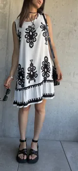 Vestido corto blanco con estampado de flores negras, corte suelto y ruedo con volantes.
