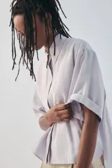 Camisa de manga corta color marrón oscuro, con cuello solapa, corte fluido y cierre frontal oculto con botones.