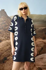 Vestido corto de punto jacquard color azul marino, con diseño de estrellas blancas alineadas verticalmente en los laterales. Presenta cuello polo con cierre frontal de botones y mangas cortas con detalles de rayas en contraste.