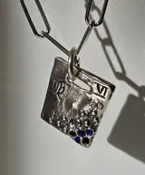 Collar de plata 950 con cadena de eslabones tipo clip y dije rectangular con diseño astrológico grabado y detalles de piedras azules.