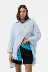 Camisa de lino celeste, de corte amplio y relajado, con cuello camisero, cierre frontal de botones y mangas largas con presilla para arremangar.
