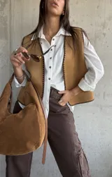 Chaleco de gamuza color camel con bordes decorativos en punto festón de color marrón oscuro. Presenta un diseño sin mangas con escote en V y cierre frontal abierto.