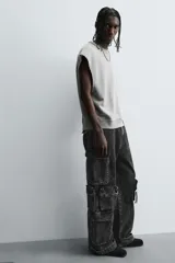 Pantalón cargo de denim lavado negro, corte relajado y tiro medio. Presenta múltiples bolsillos cargo con solapa y detalle de cierre en las perneras, además de bolsillos de vivo traseros. El bajo es ajustable con trabilla.