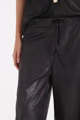 Pantalon de corte recto y holgado, confeccionado en material engomado de acabado satinado en color negro.