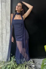 Vestido largo de color azul marino con base de crepé asimétrica y sobrecapa de microtul translúcido. Presenta un diseño de escote recto sin breteles y falda con transparencia. Incluye un accesorio de tela a juego versátil para usar como chal o lazo al cuello.
