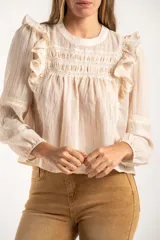 Blusa de color arena con diseño de volados en los hombros, detalle de fruncido en el pecho y mangas largas con puños elásticos.
