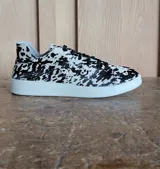 Zapatillas urbanas con estampado animal print tipo vaca en blanco y negro, con cordones negros y suela de plataforma blanca.