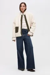 Campera de sherpa doble faz en color crema con detalles en verde oliva. Presenta cierre frontal con botones, bolsillos laterales de nylon capitoneado y terminaciones en contratono. Diseño de calce relajado con bordado en la manga.