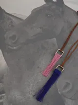 Collar con cordón de cuero marrón y dije cuadrado metálico plateado del cual cuelga una borla de hilos de seda en color azul.