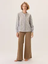 Camisa de algodón color gris claro, con cuello mao, cierre frontal de botones y mangas largas. Presenta un estampado sutil de hojas y flores, y detalles de bordado calado en los hombros.