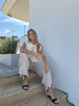 Pantalón de punto color beige, de corte ancho y largo hasta el tobillo, con diseño abstracto bordado en blanco en la parte inferior de la pierna izquierda.