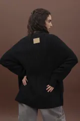 Sweater de punto negro con diseño de trenzas verticales, cuello alto y corte holgado de estilo oversize.