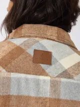 Sobrecamisa de estilo leñador con estampado de cuadros en tonos marrones, beige y gris. Presenta cuello clásico, cierre frontal con botones, bolsillos delanteros y puños tejidos acanalados. El interior está forrado con tejido tipo sherpa para mayor abrigo.