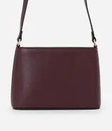 Cartera bandolera pequeña de formato rectangular, confeccionada en poliuretano con acabado liso. Presenta una correa larga ajustable, cierre superior con cremallera y un pequeño aplique metálico dorado con el logo de la marca en el frente.