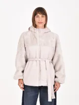 Campera gris claro con capucha, mangas y parte superior de tejido tipo borrego, y parte inferior acolchada con cinturón para ajustar en la cintura. Cierre frontal con cremallera.