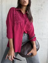 Camisa de color bordó con cuello clásico y cierre frontal de botones. Presenta un diseño distintivo con paneles de encaje bordado en la parte superior delantera, mangas largas con puños y un corte recto.
