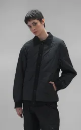 Campera tipo sobrecamisa de diseño oversize, confeccionada en microfibra opaca con patrón matelaseado geométrico. Presenta cuello, puños, cartera central y ruedo en gabardina de algodón, con cierre frontal mediante broches a presión. El diseño del ruedo simula una prenda superpuesta.