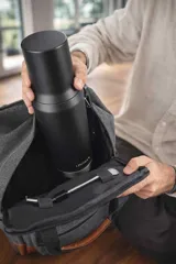 Mochila matera y porta notebook en tela canvas de color marrón, con diseño funcional que incluye bolsillo frontal con cierre, correas ajustables, manija superior y detalles de tiras de lona con hebillas metálicas.