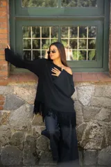 Buzo de punto color negro, con diseño oversize, cuello redondo y mangas largas. Presenta un detalle de flecos en el ruedo inferior que aporta movimiento a la prenda.