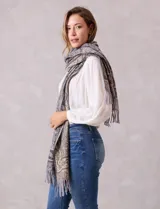 Bufandón de tejido suave con estampado de arabescos en tonos grises y beige, con terminación de flecos en los extremos.