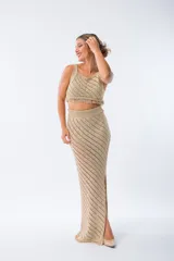 Pollera larga de tejido de punto con diseño de calados diagonales, cintura elástica y tajo lateral. Presenta terminaciones con flecos en el ruedo.