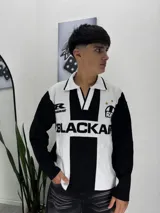 Sweater de punto con diseño inspirado en camisetas de fútbol, en colores blanco y negro. Presenta cuello polo, mangas largas y estampado frontal con la palabra 'BLACKAIR'.