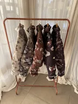 Campera puffer color marrón habano con estampado de loros, estrellas y elementos botánicos, cuello alto y cierre frontal.