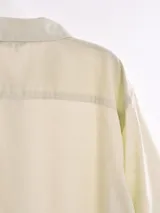 Camisa de manga corta color blanco roto con textura de tejido de lino o similar, corte holgado y cuello camisero.