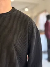 Buzo oversize de tejido waffle en color beige, con cuello redondo y manga larga, con pequeña etiqueta de marca en el dobladillo inferior.