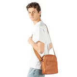 Bandolera de cuero color habano con textura granulada, cierre superior y bolsillo frontal abierto. Cuenta con una correa de tela ajustable con detalle de marca grabado.