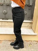 Jean mom fit de tiro alto color negro con costuras en contraste. Presenta diseño de cinco bolsillos, cierre frontal con botón metálico y costuras verticales decorativas en el frente que estilizan la figura.