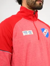 Buzo deportivo de medio cierre marca Umbro del Club Nacional de Football. Presenta un diseño en tonos azul y gris jaspeado, con cuello alto, mangas largas y detalles de costuras en contraste. Incluye el escudo del club y logo de la marca en el pecho.
