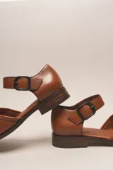 Zapato de cuero color borgoña, con puntera redondeada y diseño trenzado. Presenta una tira sobre el empeine con hebilla metálica negra.