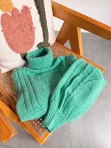 Polera de tejido de punto color verde menta, con cuello alto, diseño de trenzas y mangas abullonadas con puños ajustados.
