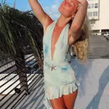 Vestido corto de microtul con estampado tipo tie-dye en tonos celestes y blancos. Presenta un escote profundo en V, diseño halter y un detalle de aplique metálico en forma de estrella de mar en la cintura. La falda incluye un volado en el ruedo y la prenda cuenta con forro interno y short incorporado.