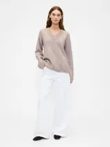 Buzo de punto con cuello en V, manga larga y puños acanalados. Diseño holgado y minimalista.