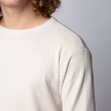 Buzo de manga larga con cuello redondo, confeccionado en tela tipo waffle de color beige. Presenta un corte long-fit con ruedo redondeado, ofreciendo un estilo relajado y moderno.